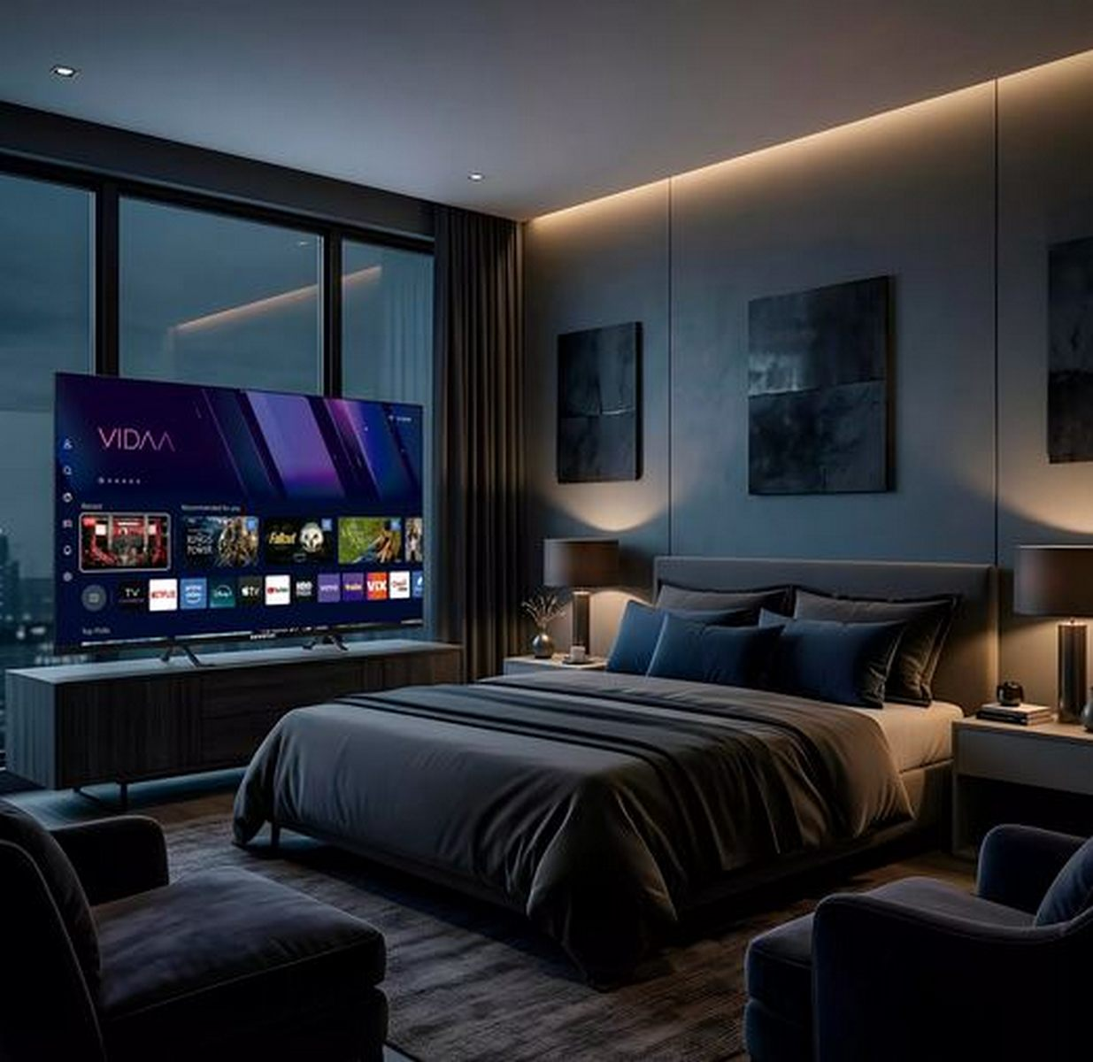 Dormitorio moderno y oscuro con gran televisor, cama hecha, dos sillones y cálida iluminación en la pared.