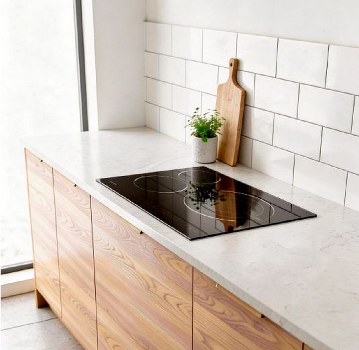 Cocina moderna con gabinetes de madera, encimera blanca, placa de inducción y salpicadero de azulejos blancos.