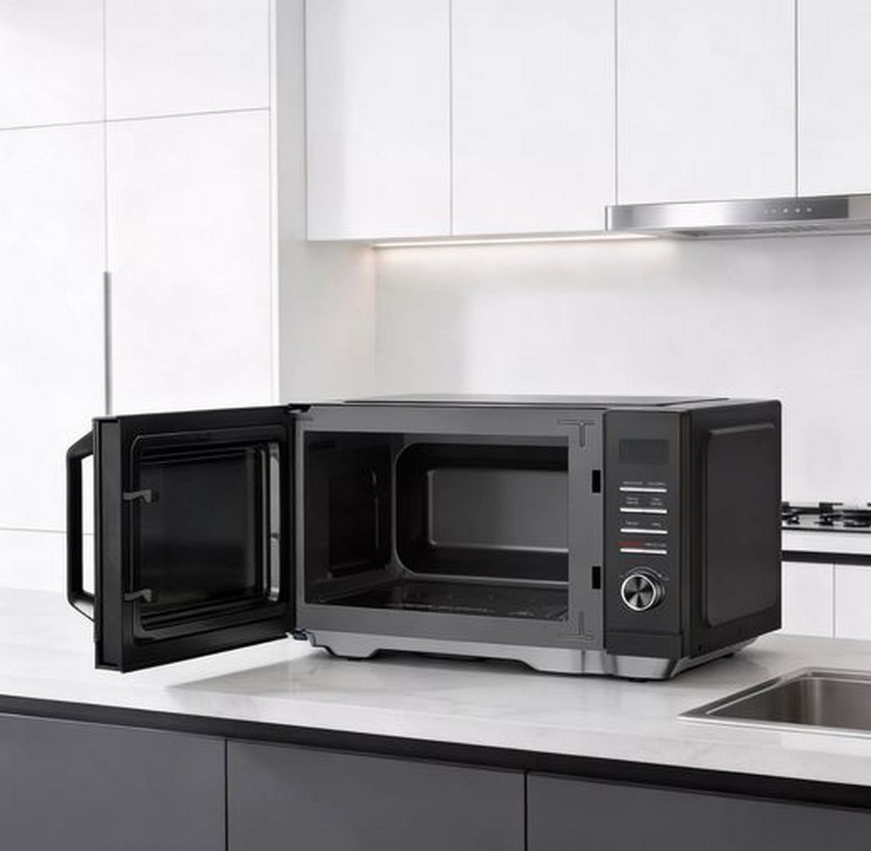 Un microondas negro con la puerta abierta sobre una encimera blanca en una cocina moderna.