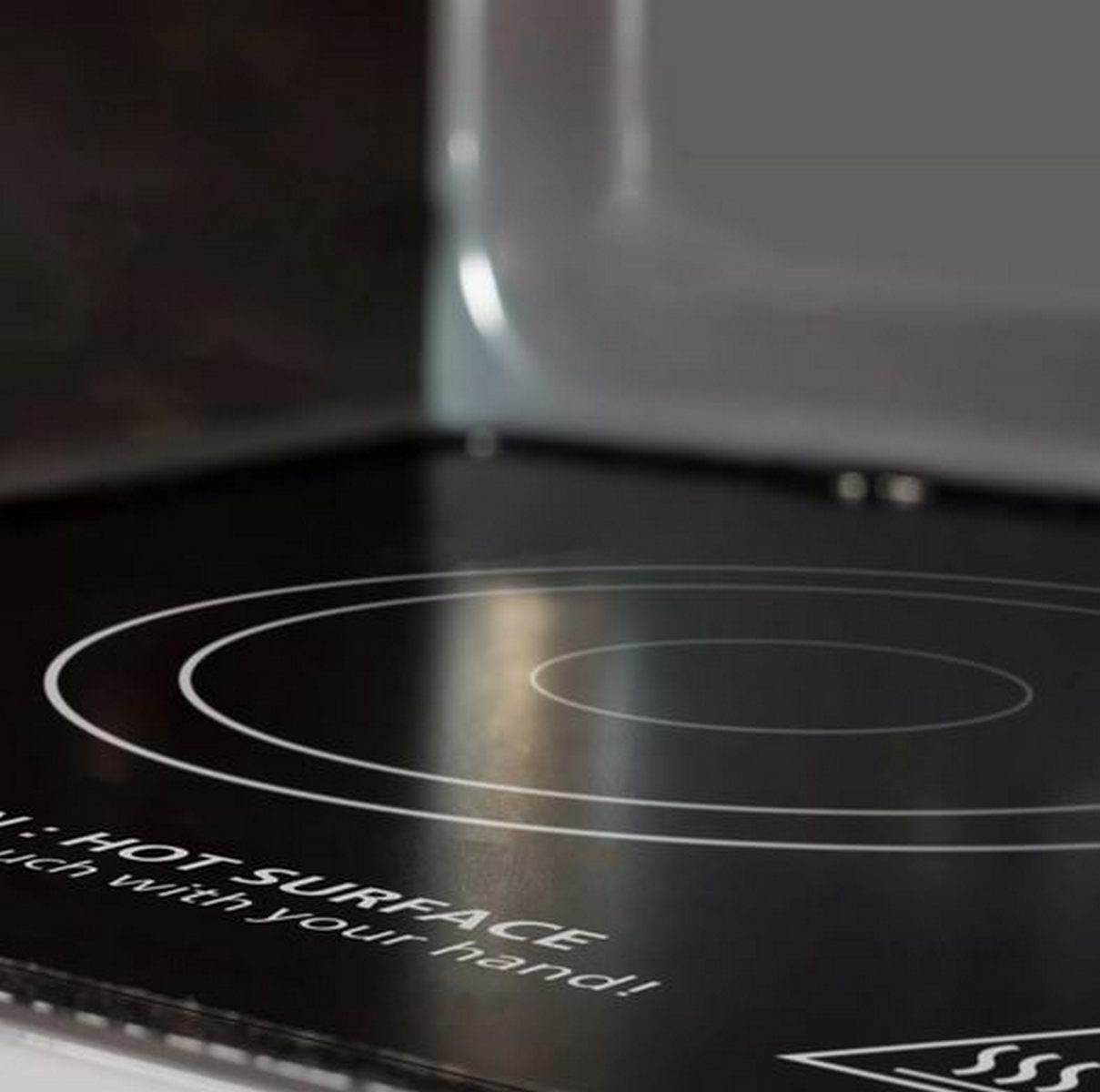 Placa de inducción negra con anillos blancos y advertencia de superficie caliente.