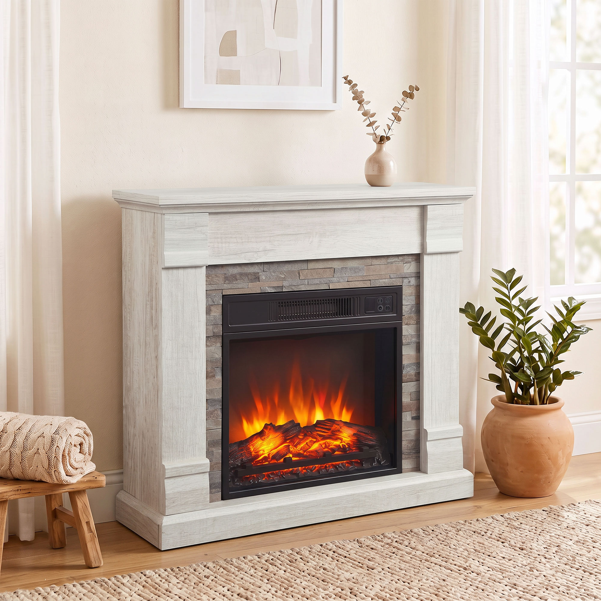 Una chimenea eléctrica blanca con detalles de piedra en una sala luminosa, decorada con jarrón y plantas.