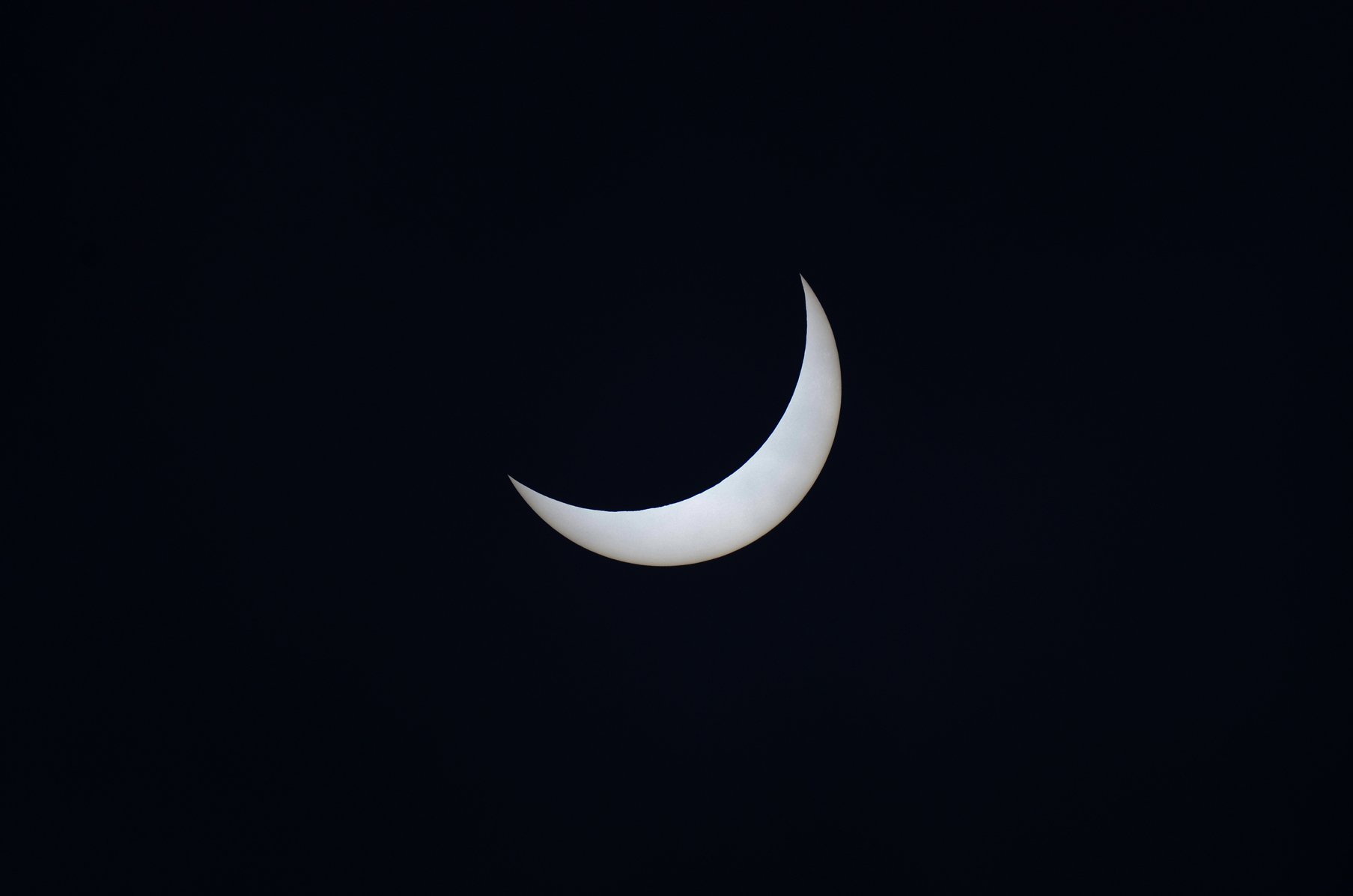 Una brillante luna creciente blanca se centra en un cielo nocturno oscuro y negro.