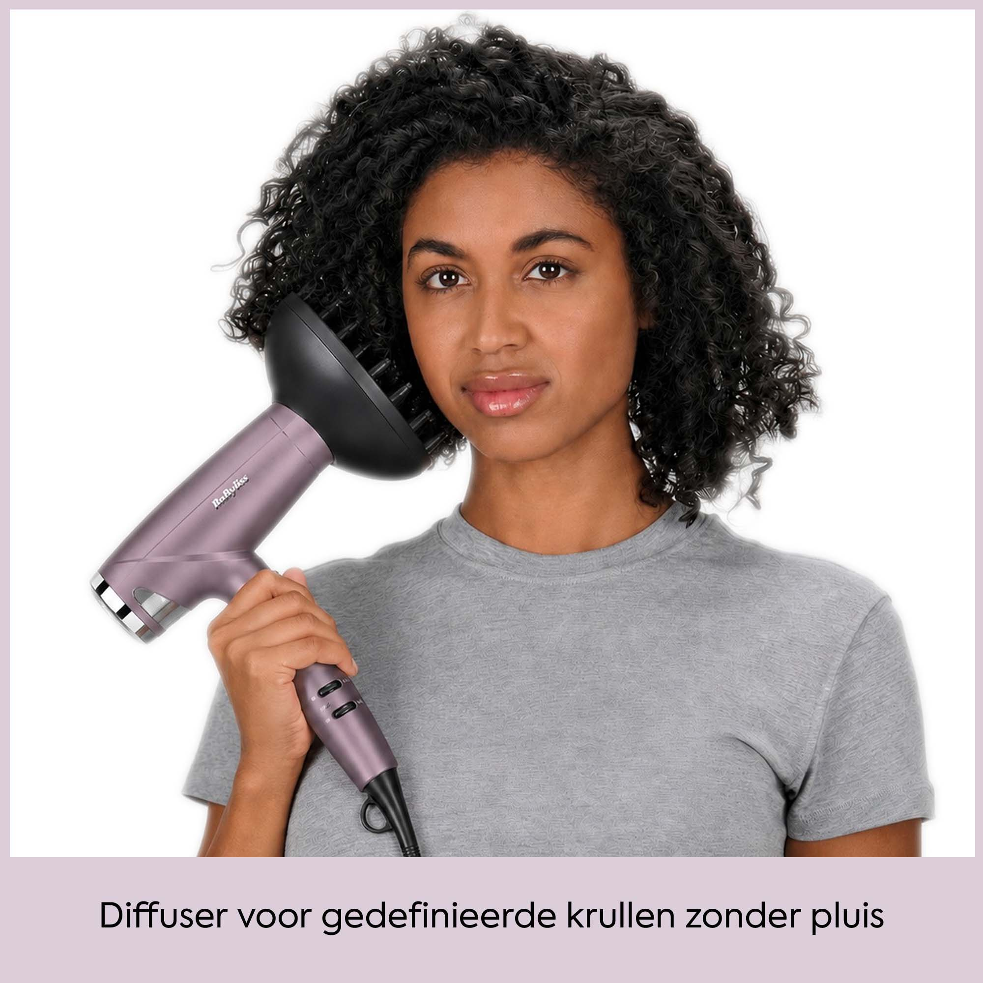 Una donna con i capelli scuri ricci tiene un asciugacapelli viola.