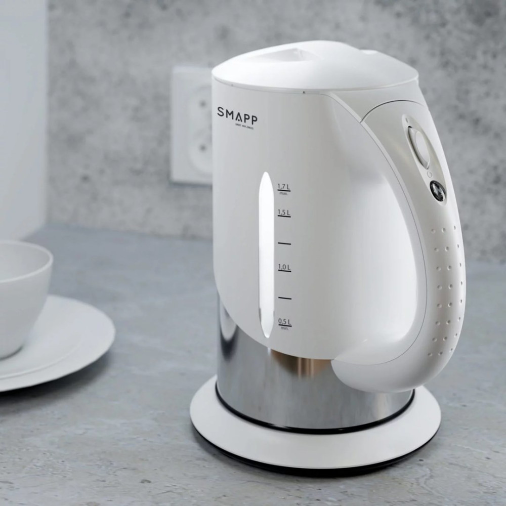 Un bollitore bianco Smapp con base in acciaio inossidabile si trova su un bancone grigio accanto a una tazza.