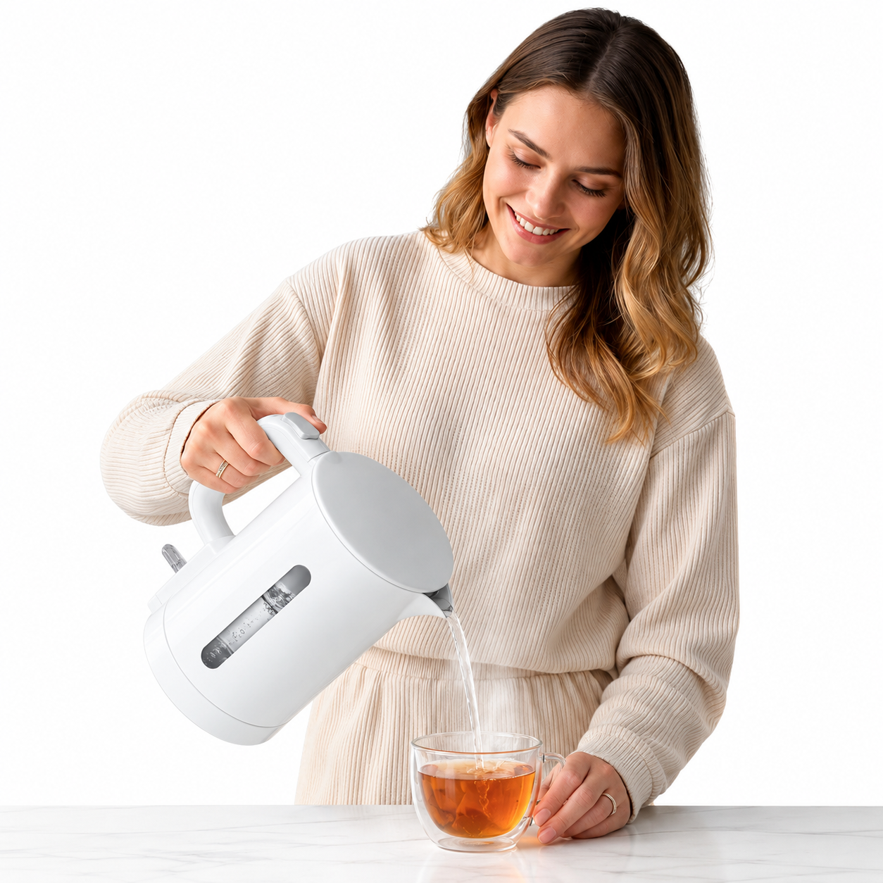Eine Frau in einem beigen Pullover gießt heißes Wasser aus einem weißen Wasserkocher in eine Tasse.