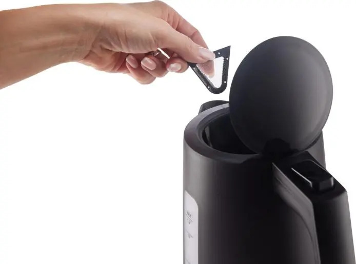 Una mano inserisce un piccolo filtro nell'apertura di un bollitore nero.