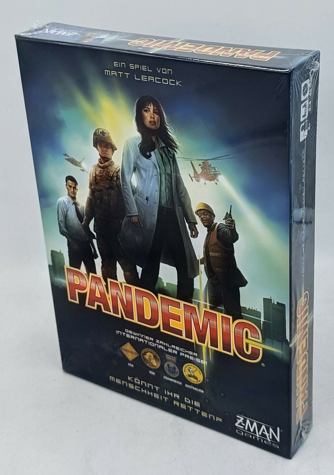 Die Brettspielbox von Pandemic zeigt vier Personen vor einer düsteren Skyline mit Hubschrauber und Flugzeug.
