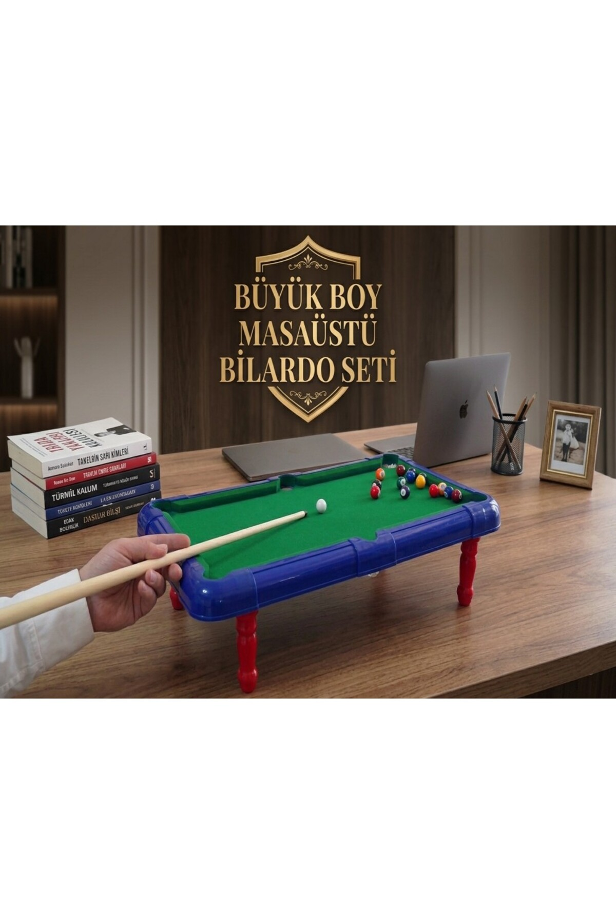 Ahşap masa üzerinde kırmızı ayaklı mavi mini bilardo seti, arka planda laptoplar ve kitaplar.