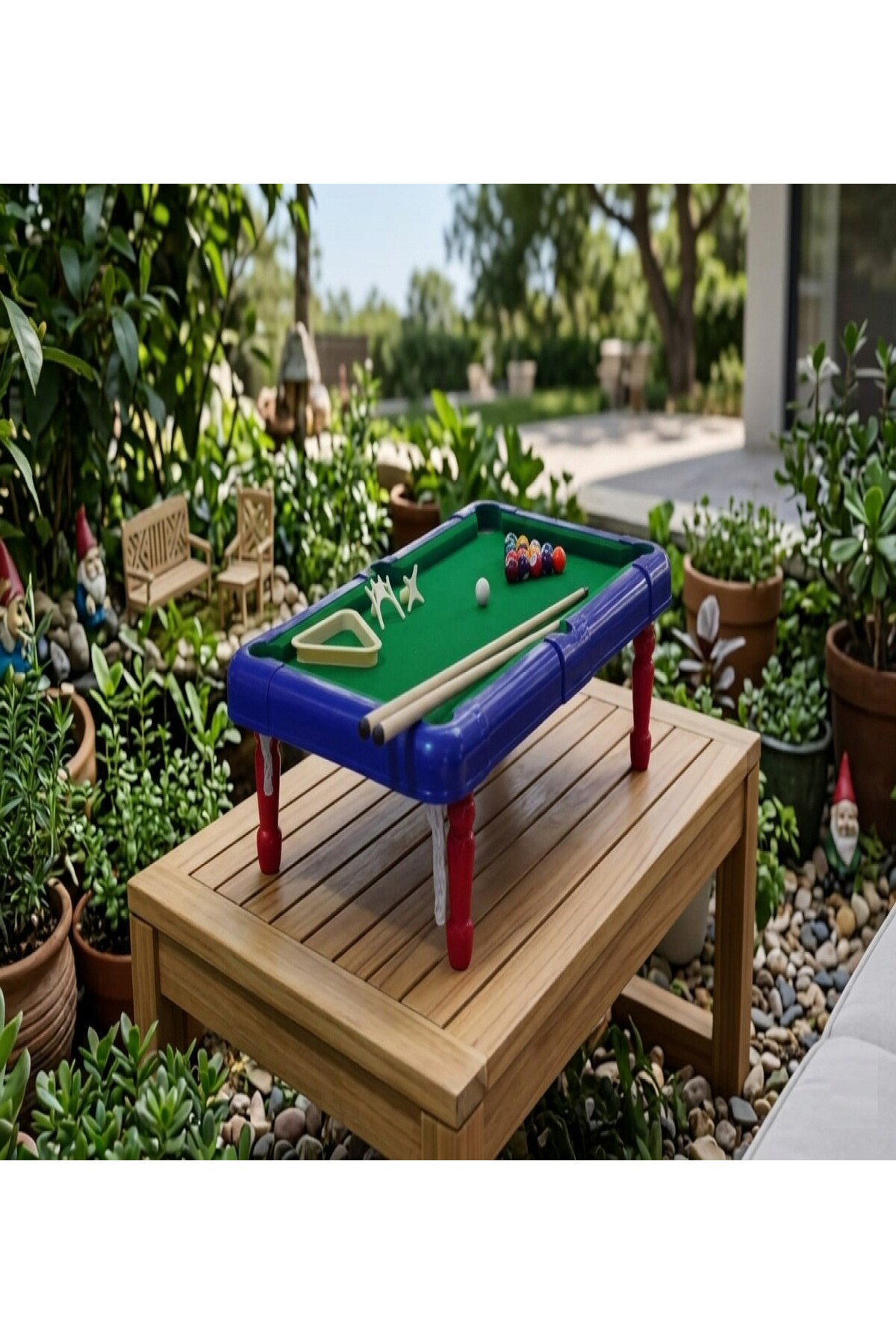 Bahçedeki ahşap bir masanın üzerinde minyatür bir bilardo masası, etrafı bitkilerle çevrili.
