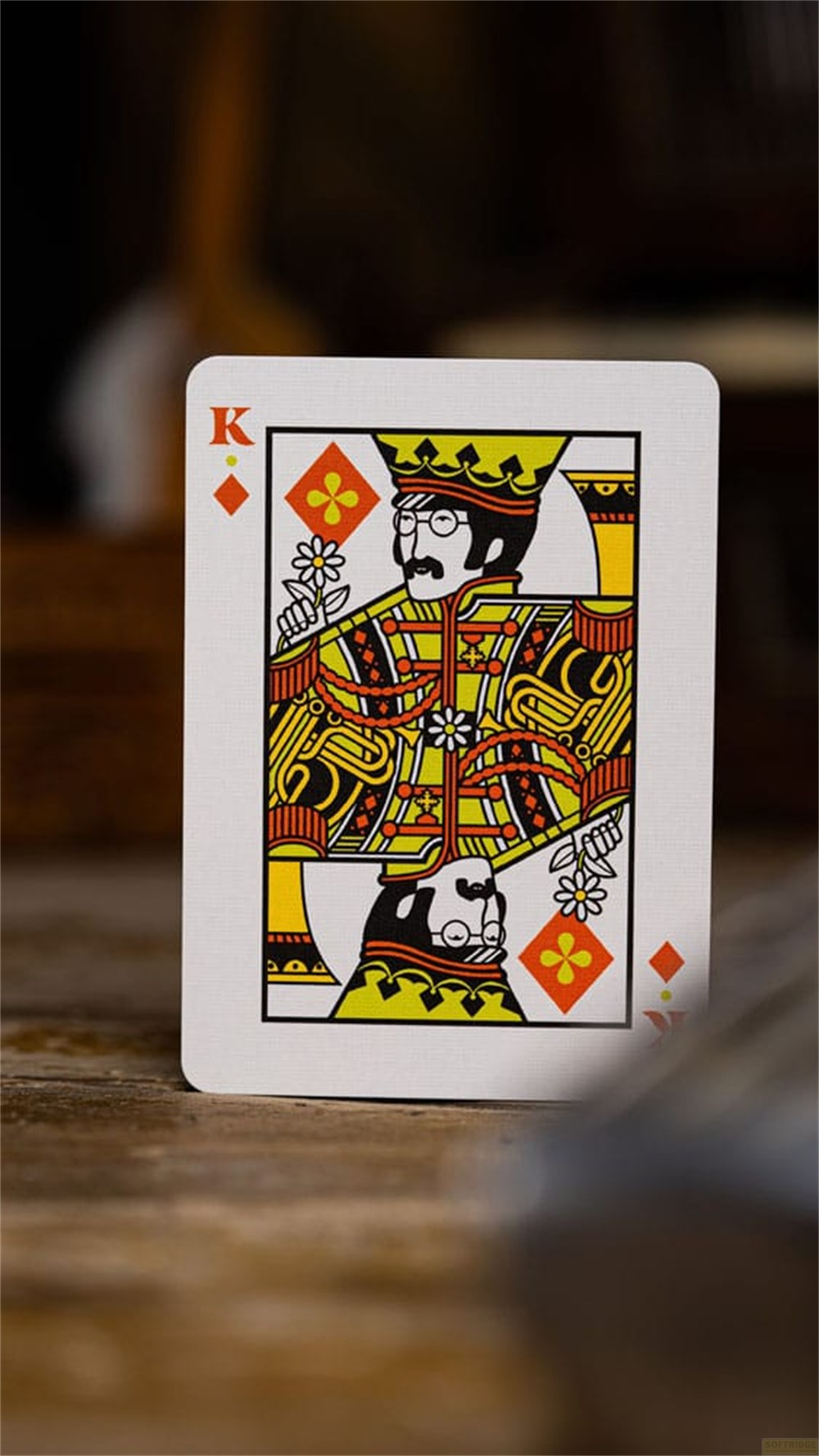 Une carte à jouer représentant le Roi de Carreau en jaune, rouge et noir, posée sur une surface en bois rustique.