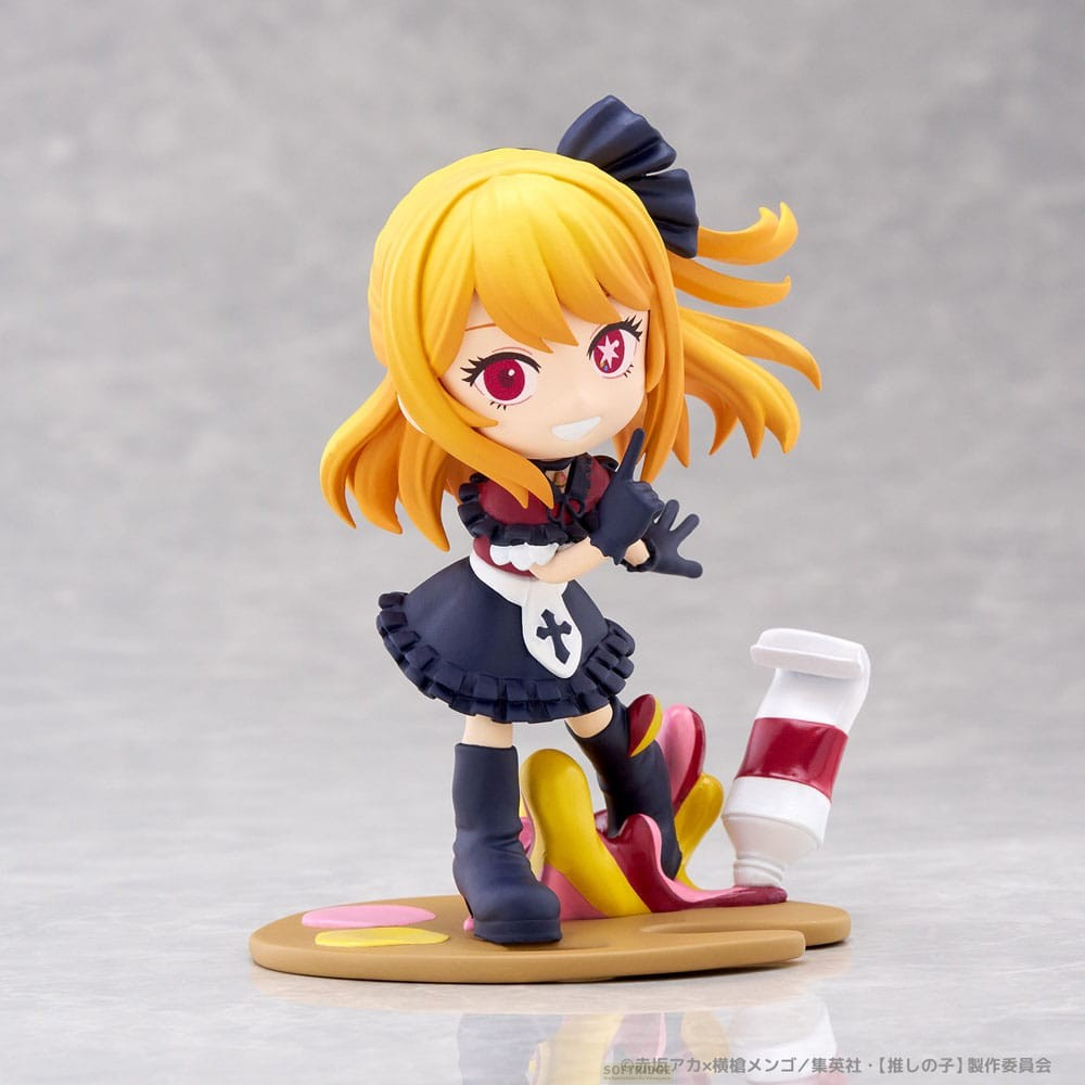 Una linda figura de anime con cabello amarillo, ojos rojos y un vestido negro y rojo sobre una paleta de pintura.