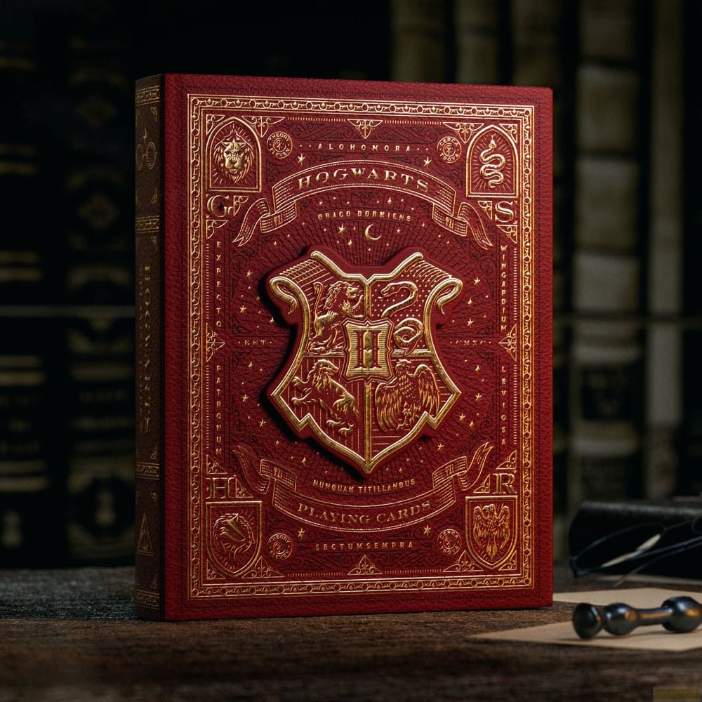 Une boîte de cartes à jouer Hogwarts rouge et or repose sur une table en bois sombre avec des livres.