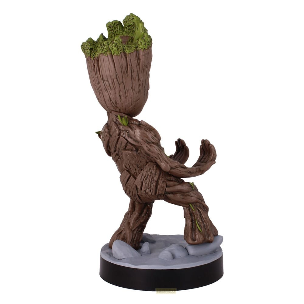 Una statuetta di legno di Groot con muschio verde sulla testa si erge su una base grigia su sfondo bianco.