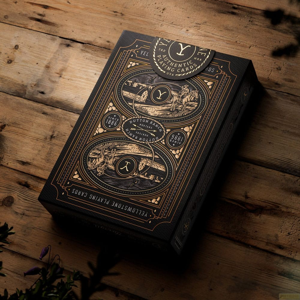 Une boîte de cartes à jouer noire Yellowstone avec des motifs dorés repose sur une table en bois.