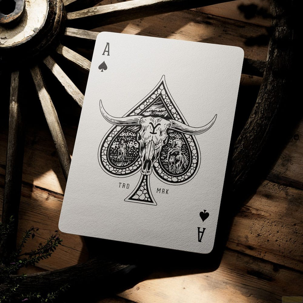 Carte à jouer avec un design d'As de Pique, crâne de taureau et roue de chariot en bois en arrière-plan.