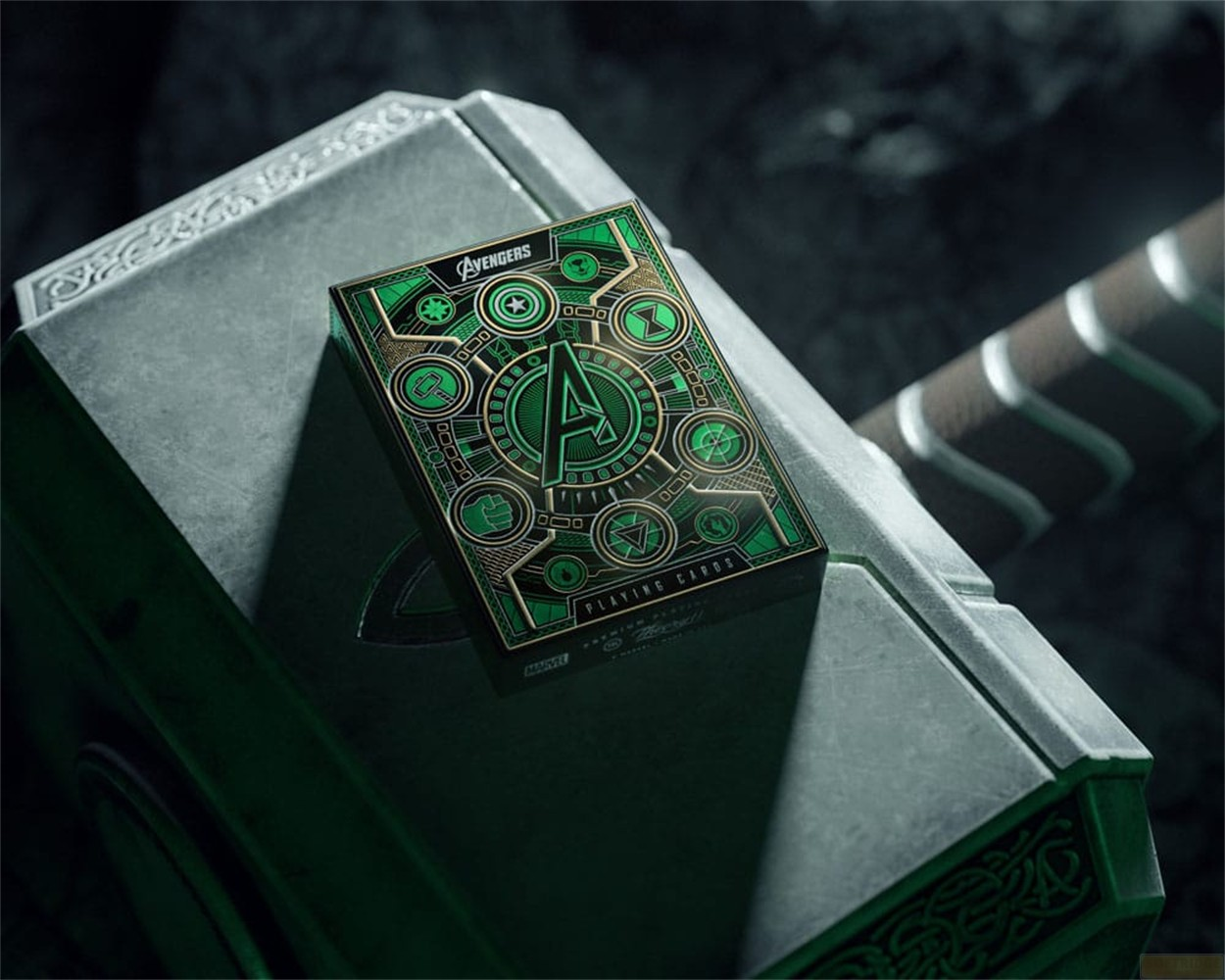 Eine Avengers-Spielkartenschachtel liegt bei gedimmtem Licht auf dem metallischen Hammer von Thor, Mjölnir.
