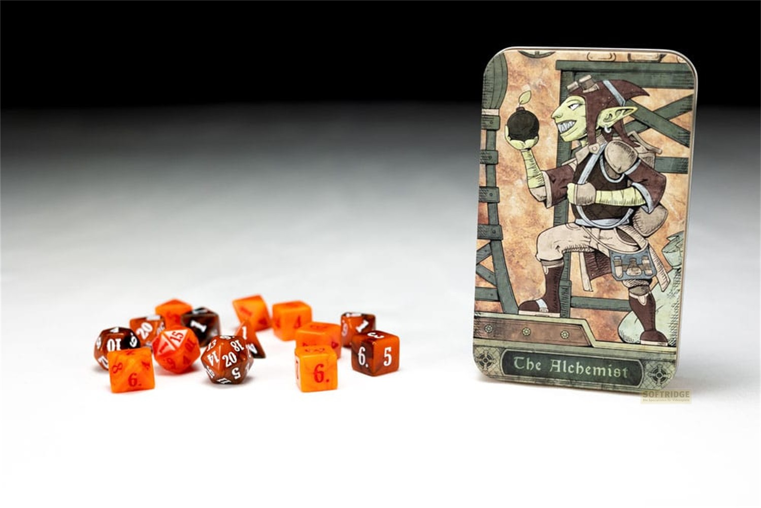 Un jeu de dés orange et marron près d'une boîte en fer-blanc illustrée d'un gobelin alchimiste.