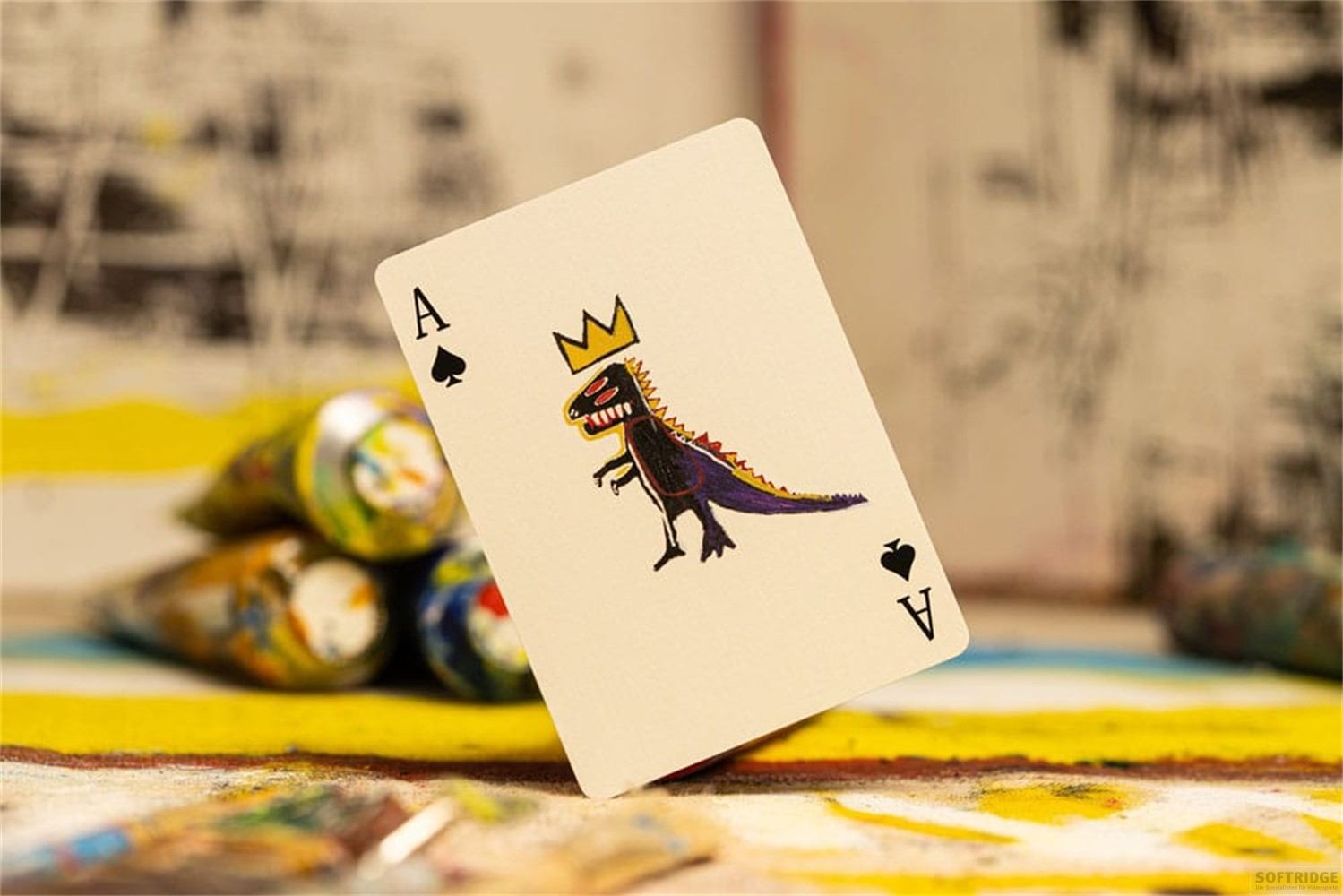 Une carte d'as de pique avec un dinosaure couronné, posée sur une surface tachée de peinture.