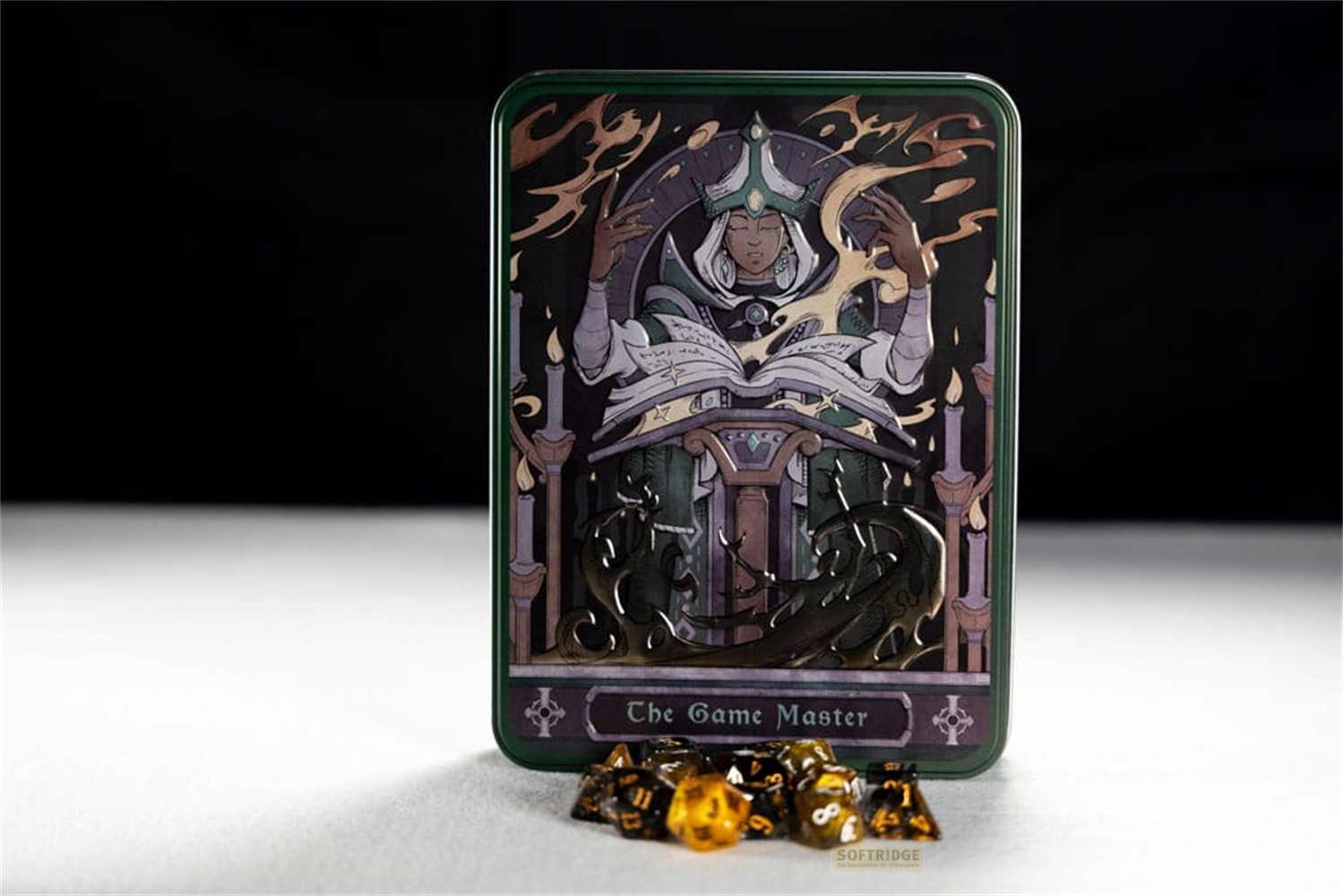 Une boîte métallique rectangulaire intitulée The Game Master est sur une table, avec des dés jaunes et noirs devant.