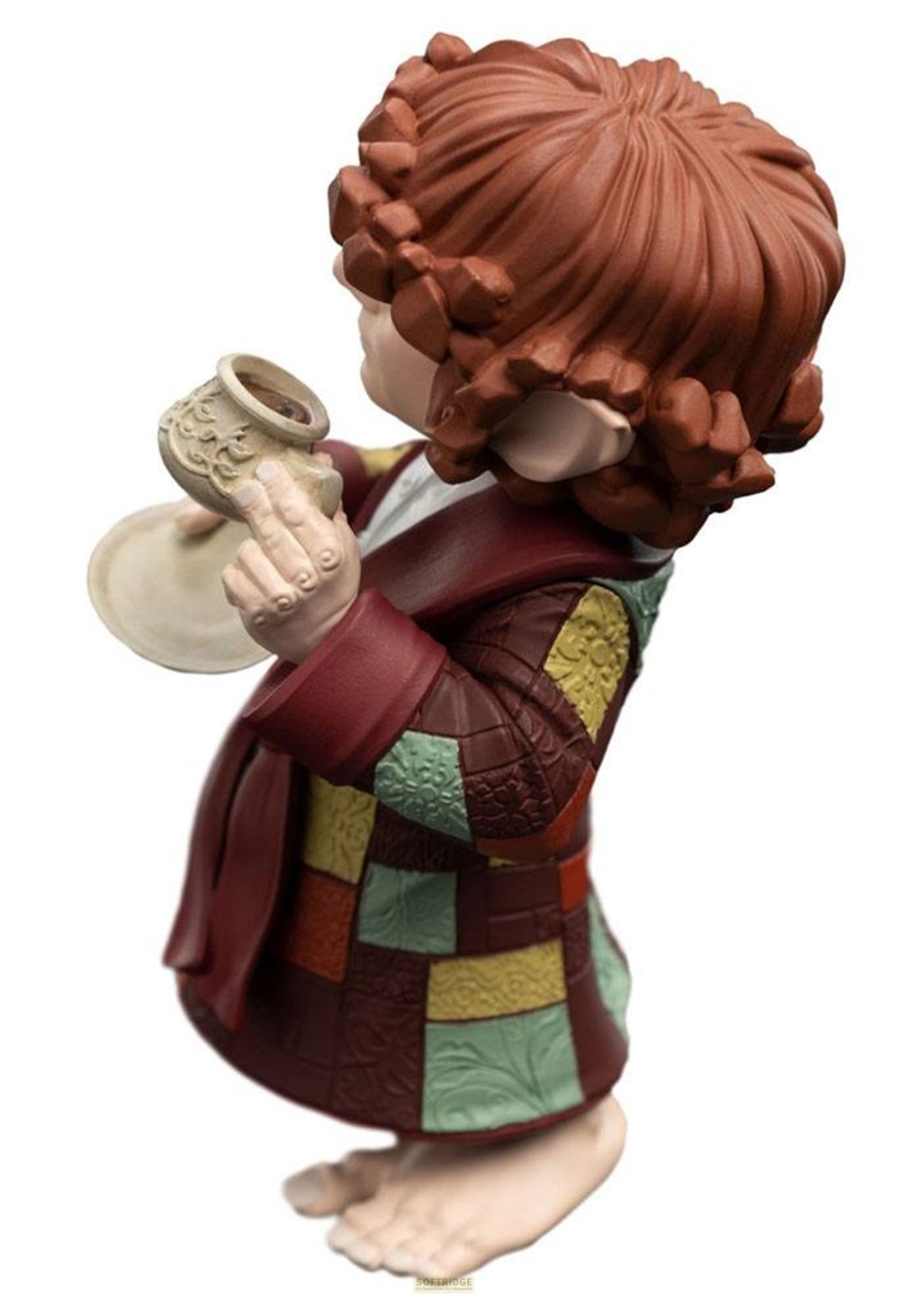 Una figura de hobbit con pelo rojizo y bata de retazos sostiene una taza pequeña y un platillo.