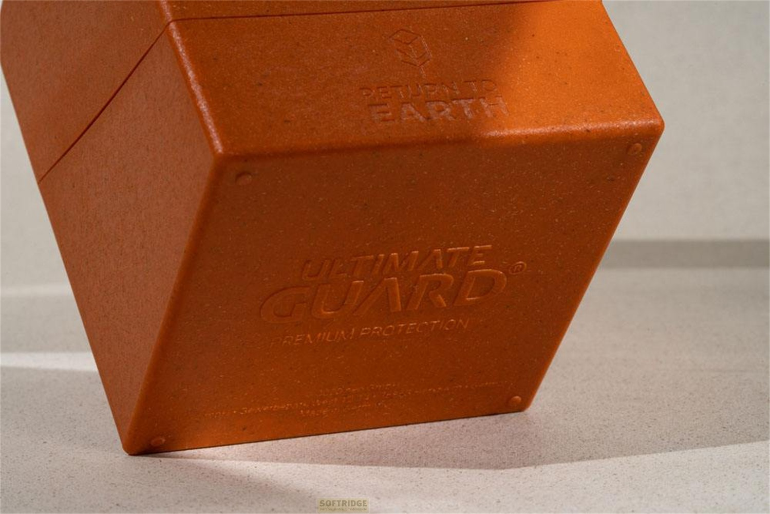 Une boîte orange Ultimate Guard avec logo en relief et texte Return to Earth sur fond beige.