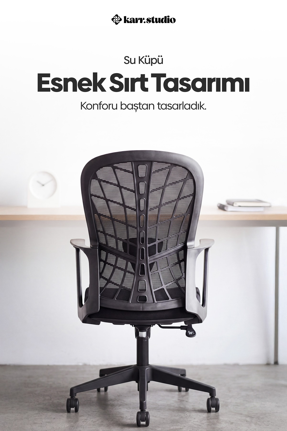 File sırtlı siyah ergonomik ofis koltuğu, saat ve kitapların olduğu beyaz çalışma masasının önünde.