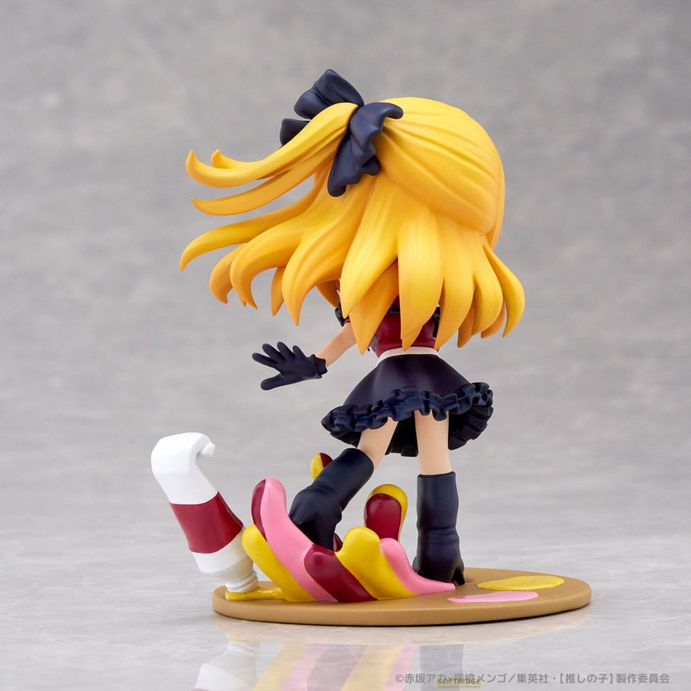 Vista trasera de una figura de anime con cabello rubio largo y un vestido oscuro pisando pintura.