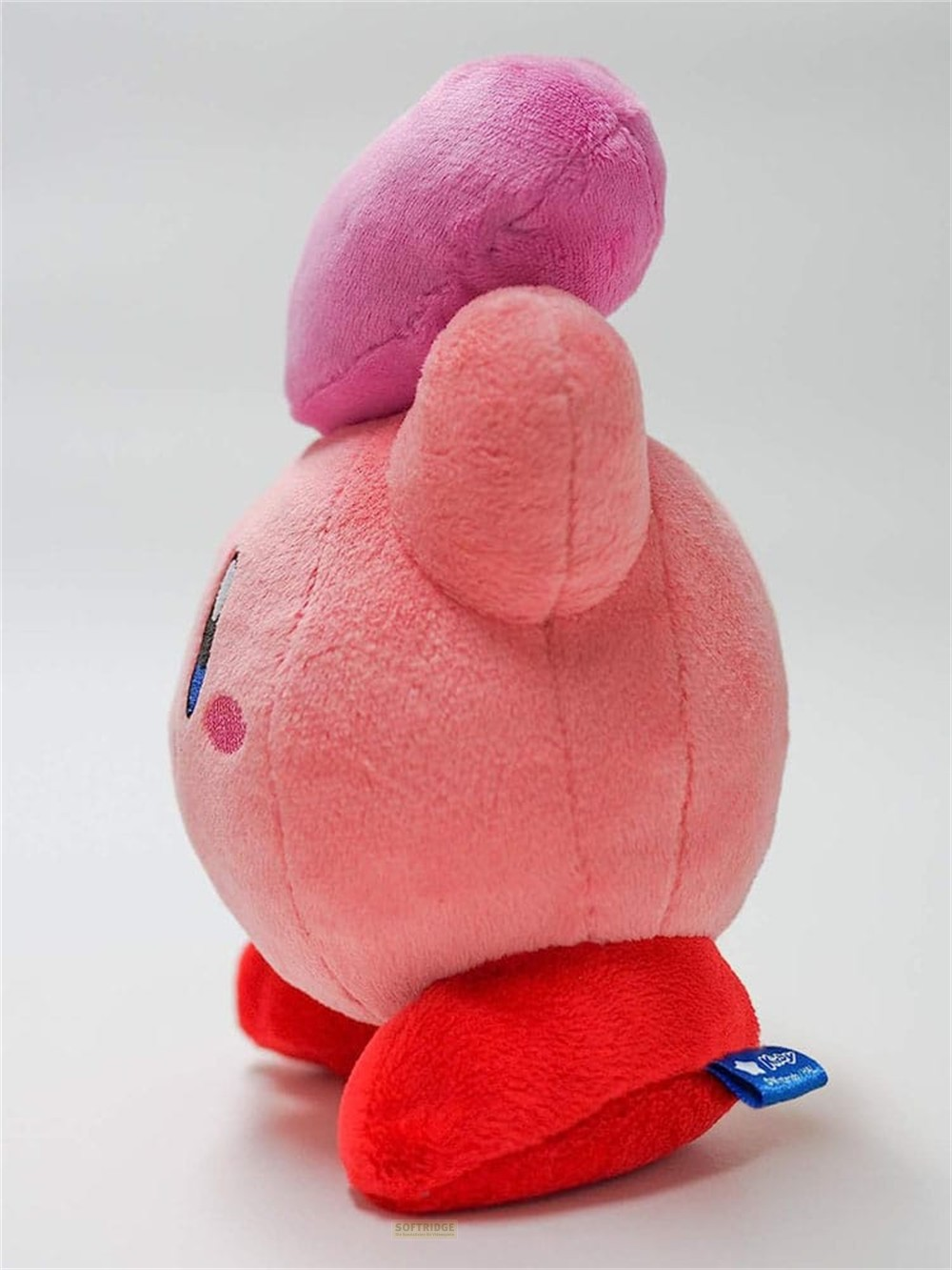 Un peluche rosa de Kirby con un corazón en la cabeza, de pie sobre pies rojos en fondo blanco.