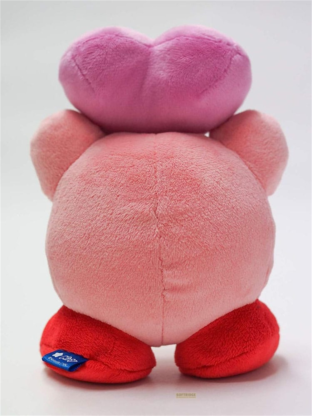 Un peluche rosa de Kirby visto desde atrás, sosteniendo un gran corazón rosa sobre su cabeza sobre un fondo blanco.
