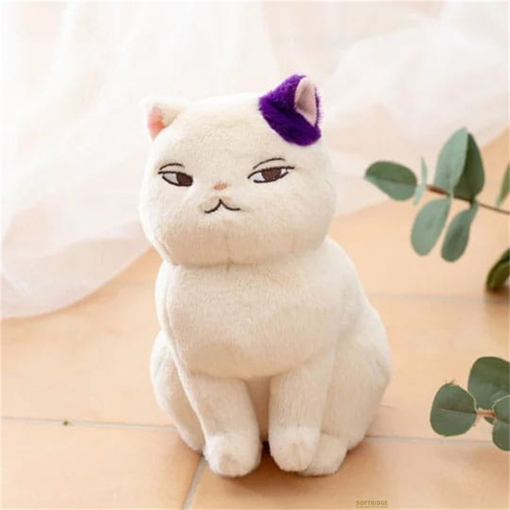 Un peluche de gato blanco con una oreja morada se sienta contra un fondo claro con hojas verdes.