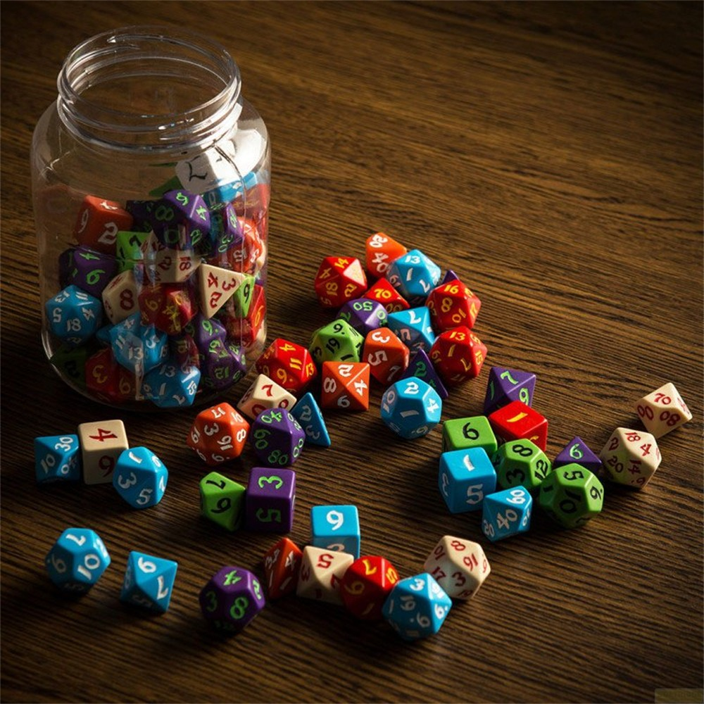 Un bocal en verre rempli de dés colorés, avec beaucoup d'autres éparpillés sur une table en bois.