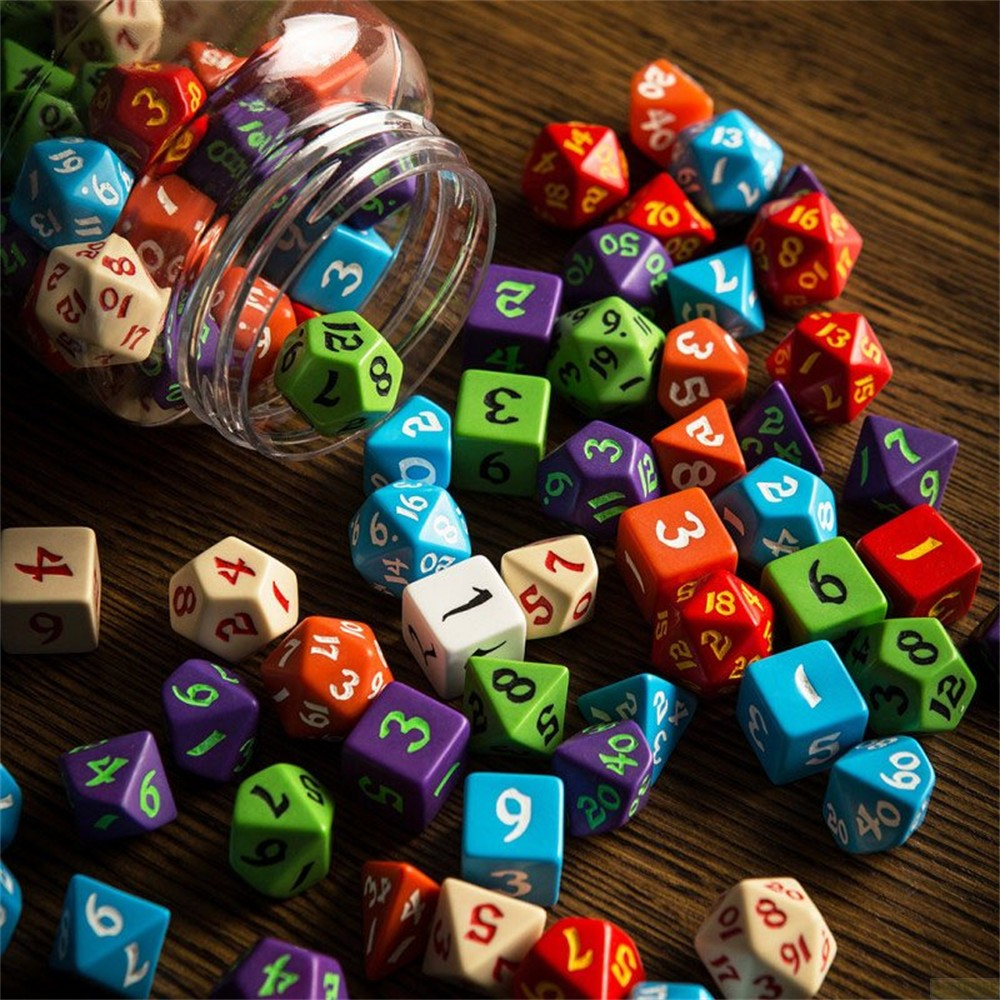 Des dés de RPG colorés et variés sont éparpillés et débordent d'un récipient en plastique transparent sur du bois.
