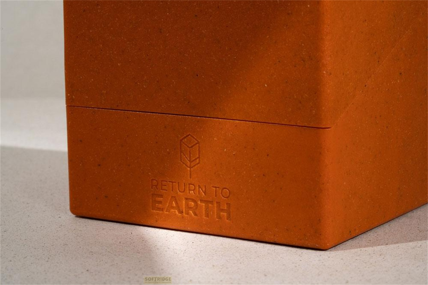 Un bloc en plastique orange avec le logo en relief et le texte Return to Earth sur une surface claire.