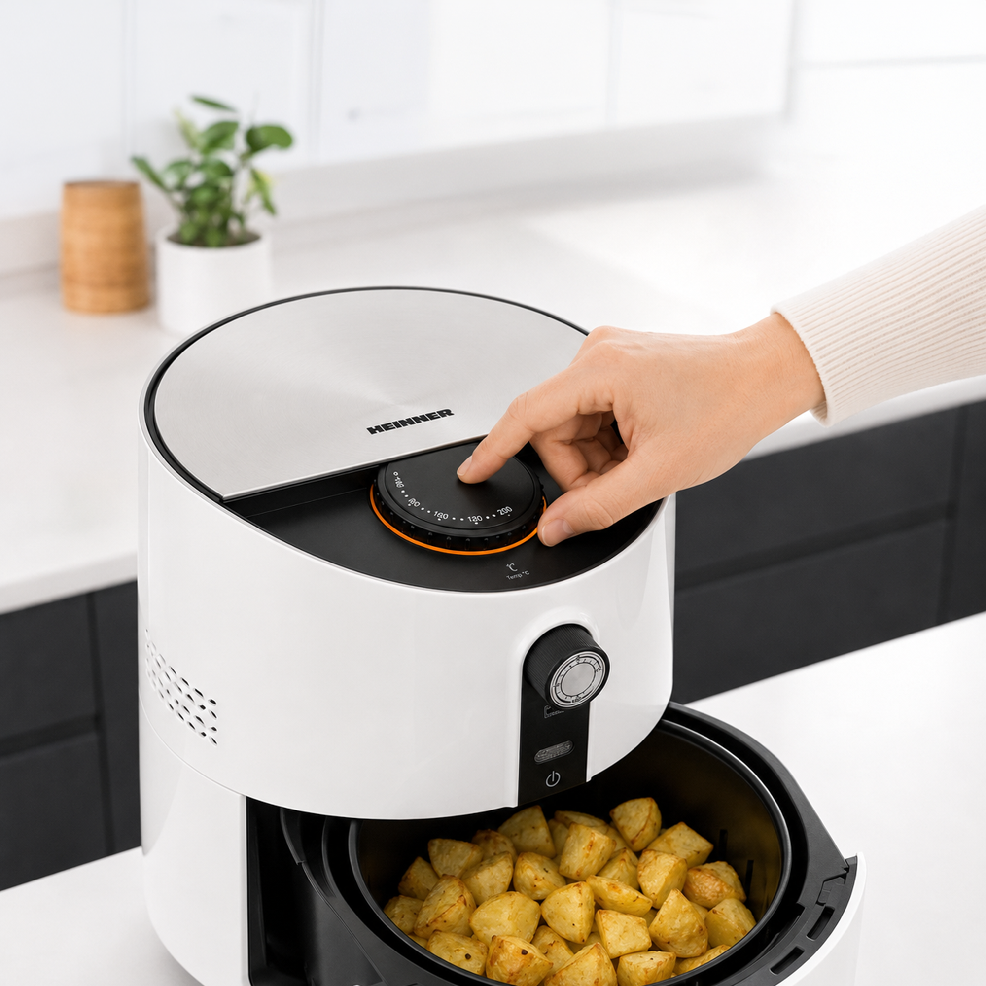 Hand adjusting temperature on a white air fryer with golden potatoes inside.