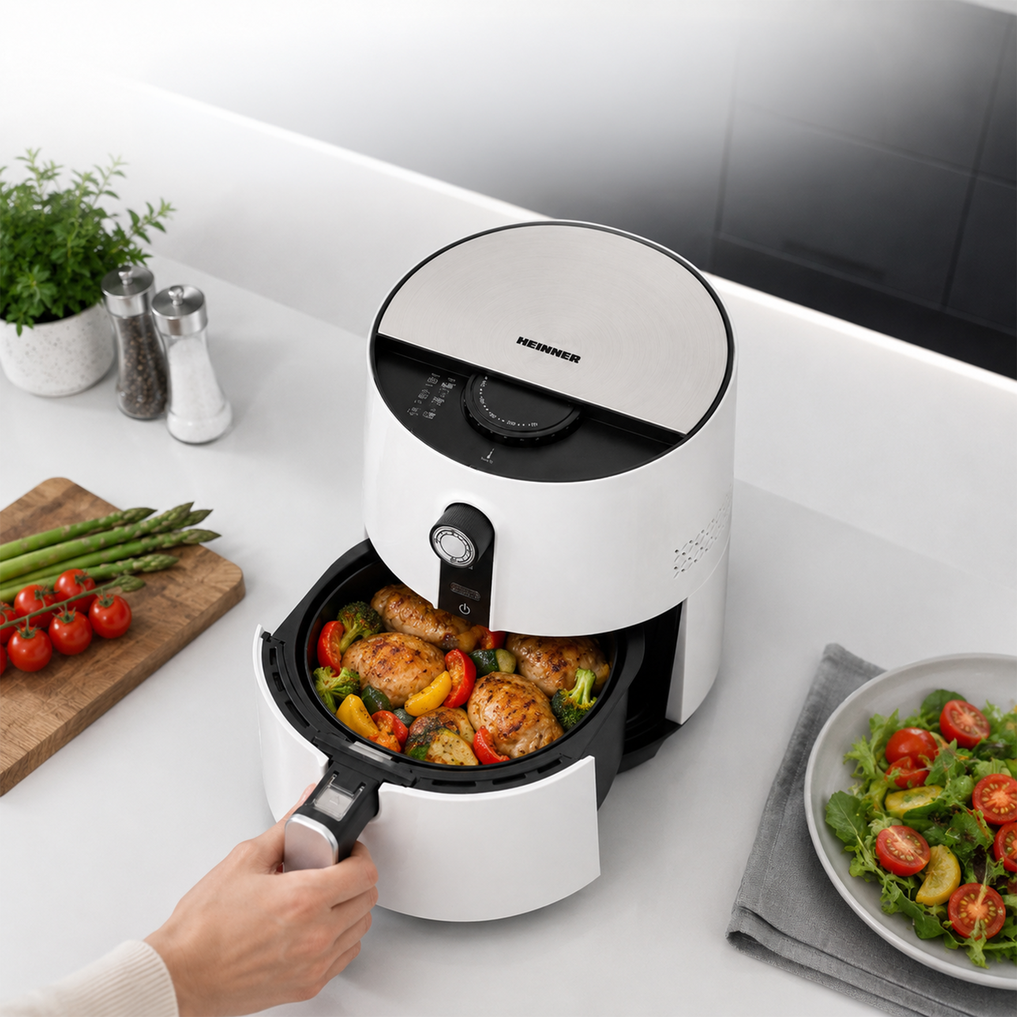 A hand pulls open the basket of a white air fryer filled with cooked chicken and vegetables.