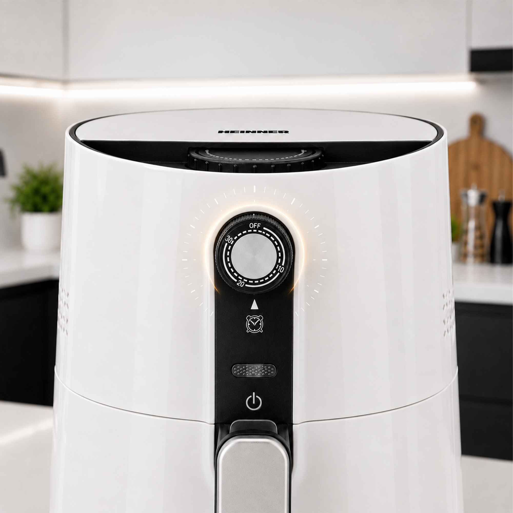 Close-up of a white air fryer with a black control panel and timer knob, set in a modern kitchen background.