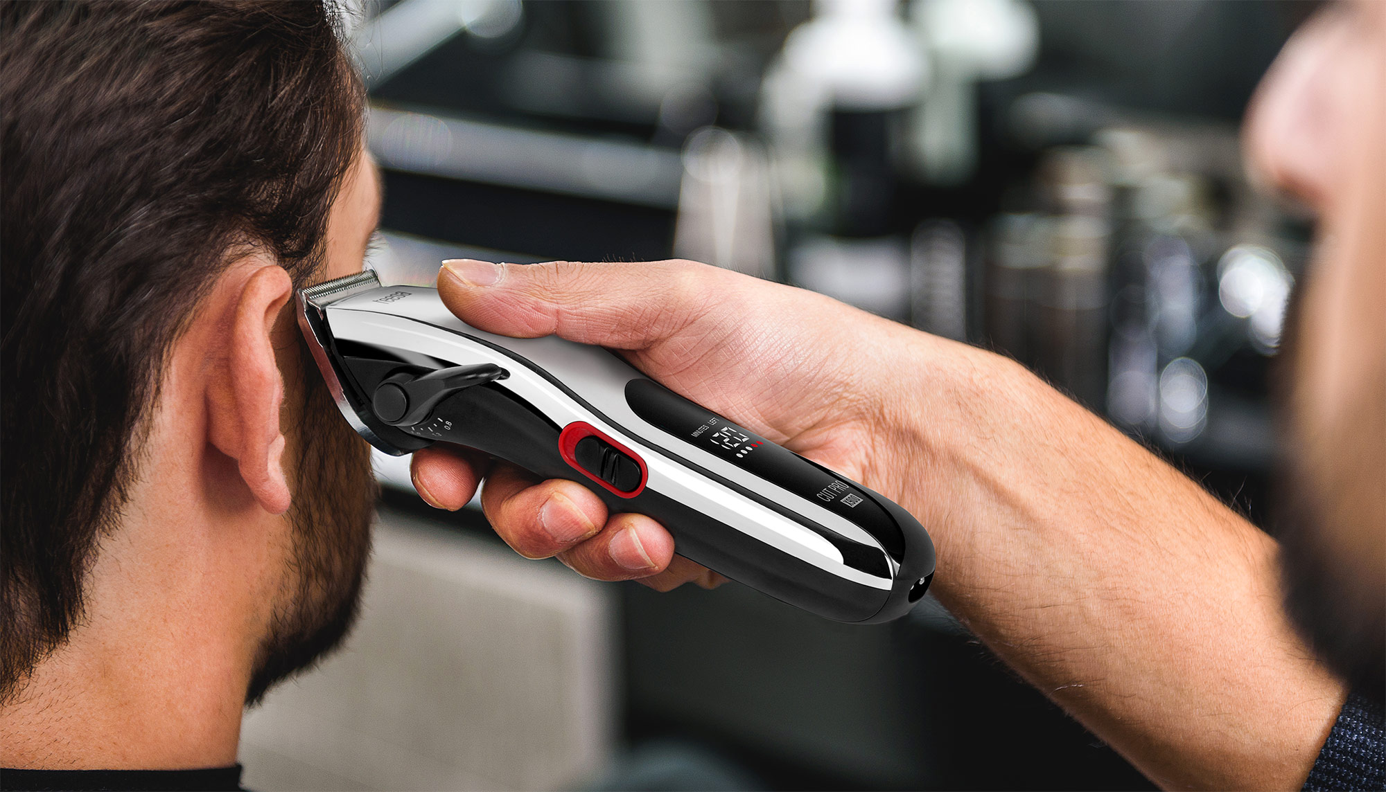 Ein Friseur trimmt mit einer Haarschneidemaschine die Koteletten eines Mannes.