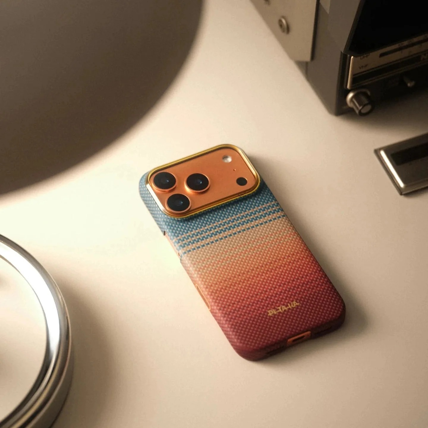 Smartfon w niebiesko-pomarańczowe wzory leży na stoliku obok lampy i radia.