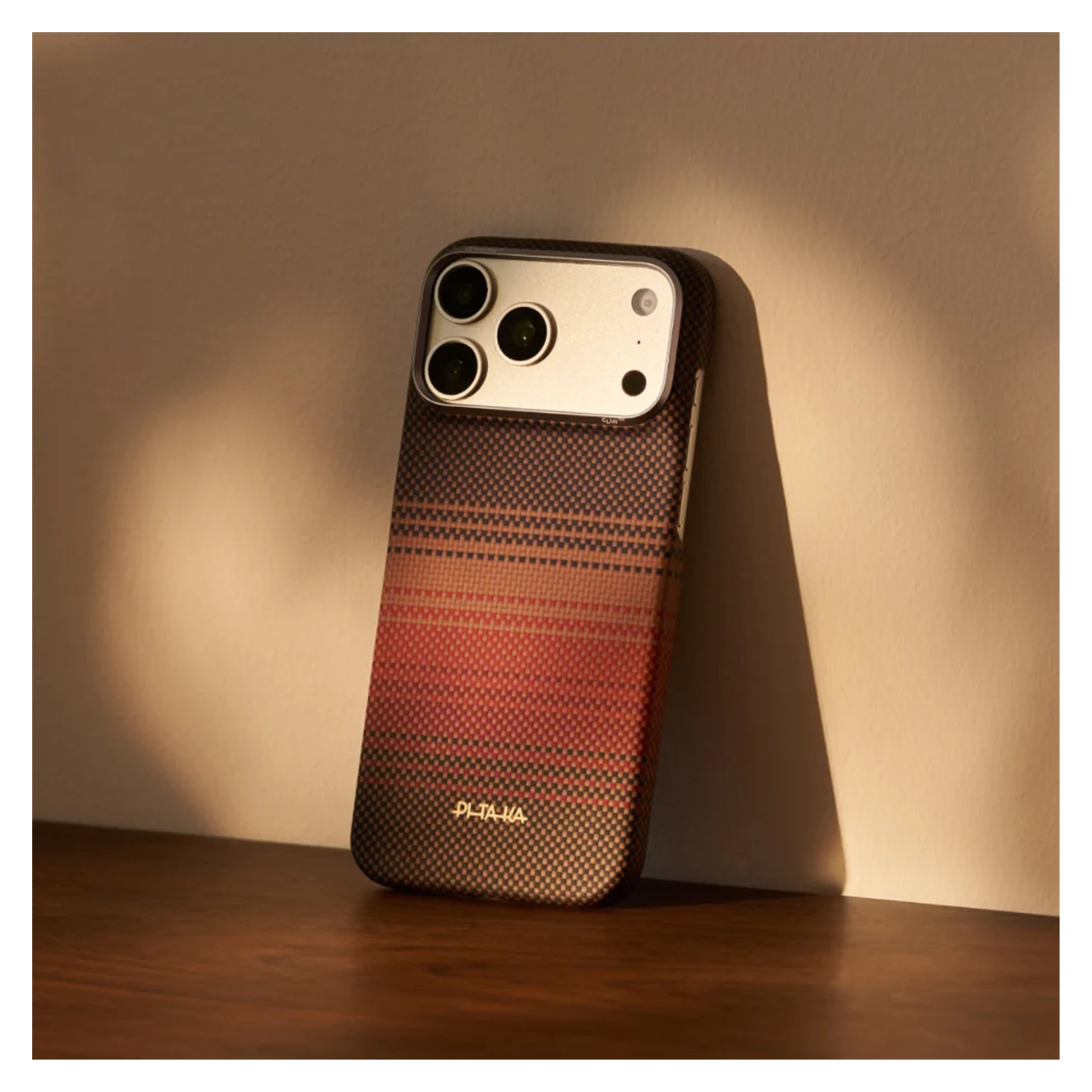 Smartfon w wzorzystym etui na ciemnym drewnie na tle beżowej ściany.
