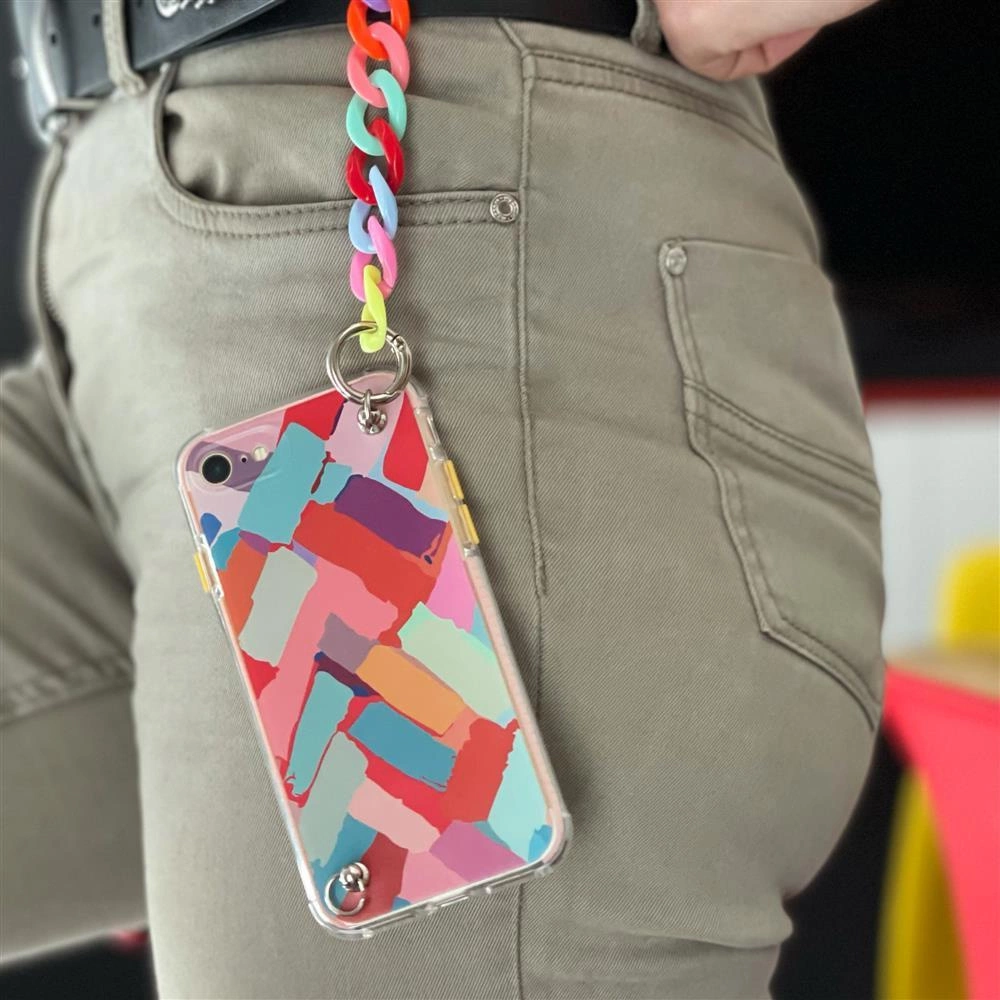 Uno smartphone con cover colorata e catenella appeso a pantaloni grigi.