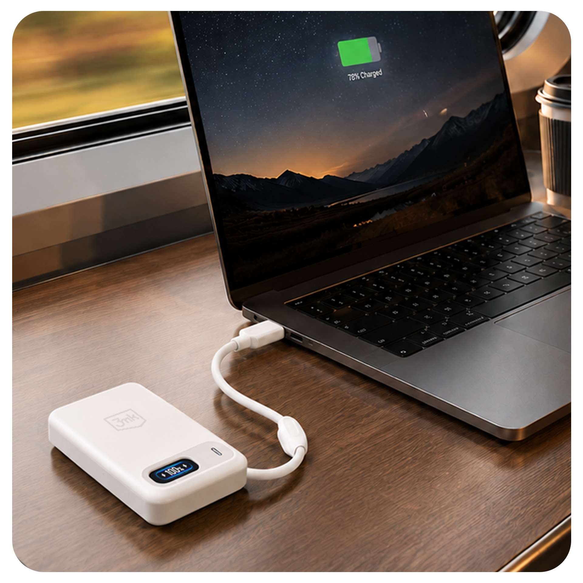 Biały powerbank ładuje laptopa na drewnianym biurku przy oknie pociągu.