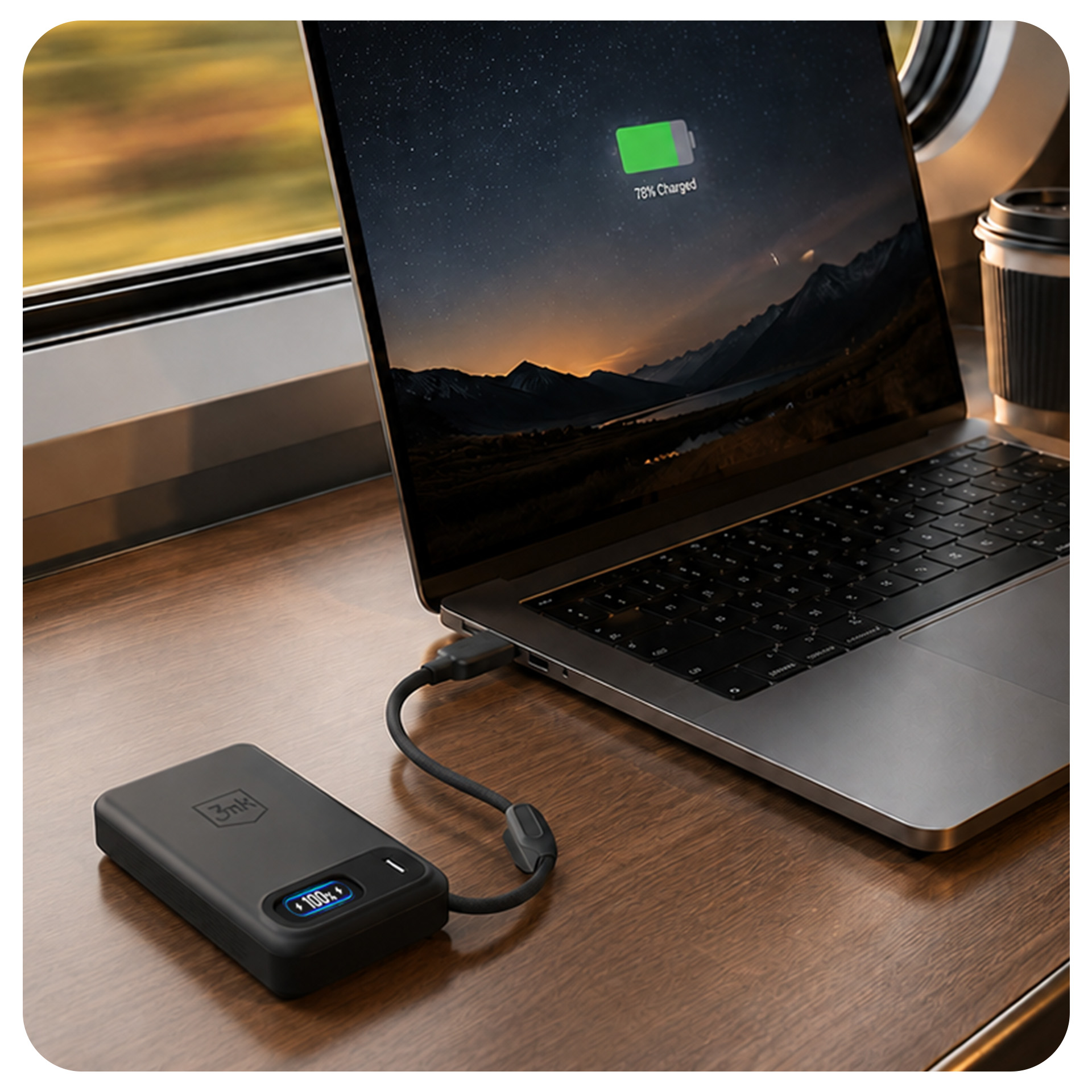Laptop ładuje się z powerbanka na drewnianym stole, obok okna pociągu.