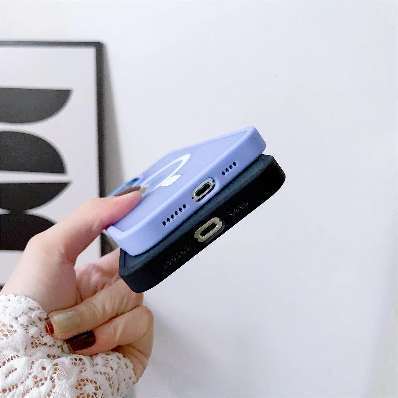 Una mano regge due cover per smartphone viola e nera davanti a una parete.