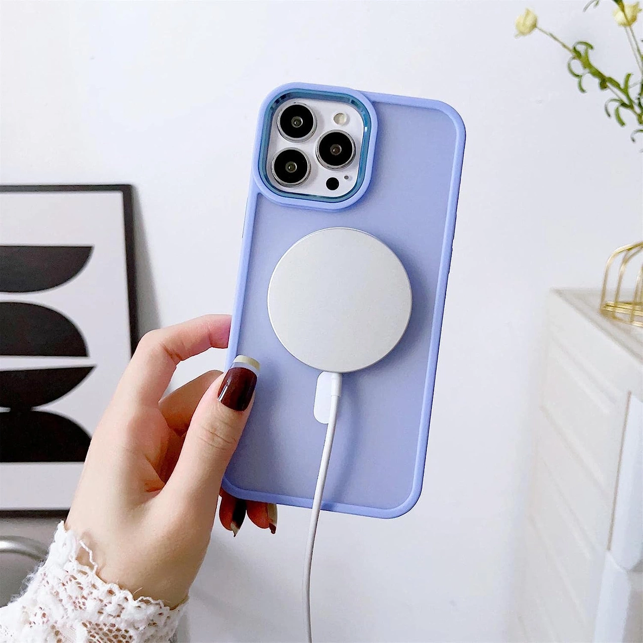 Una mano tiene un iPhone lavanda con caricabatterie MagSafe bianco su sfondo bianco.