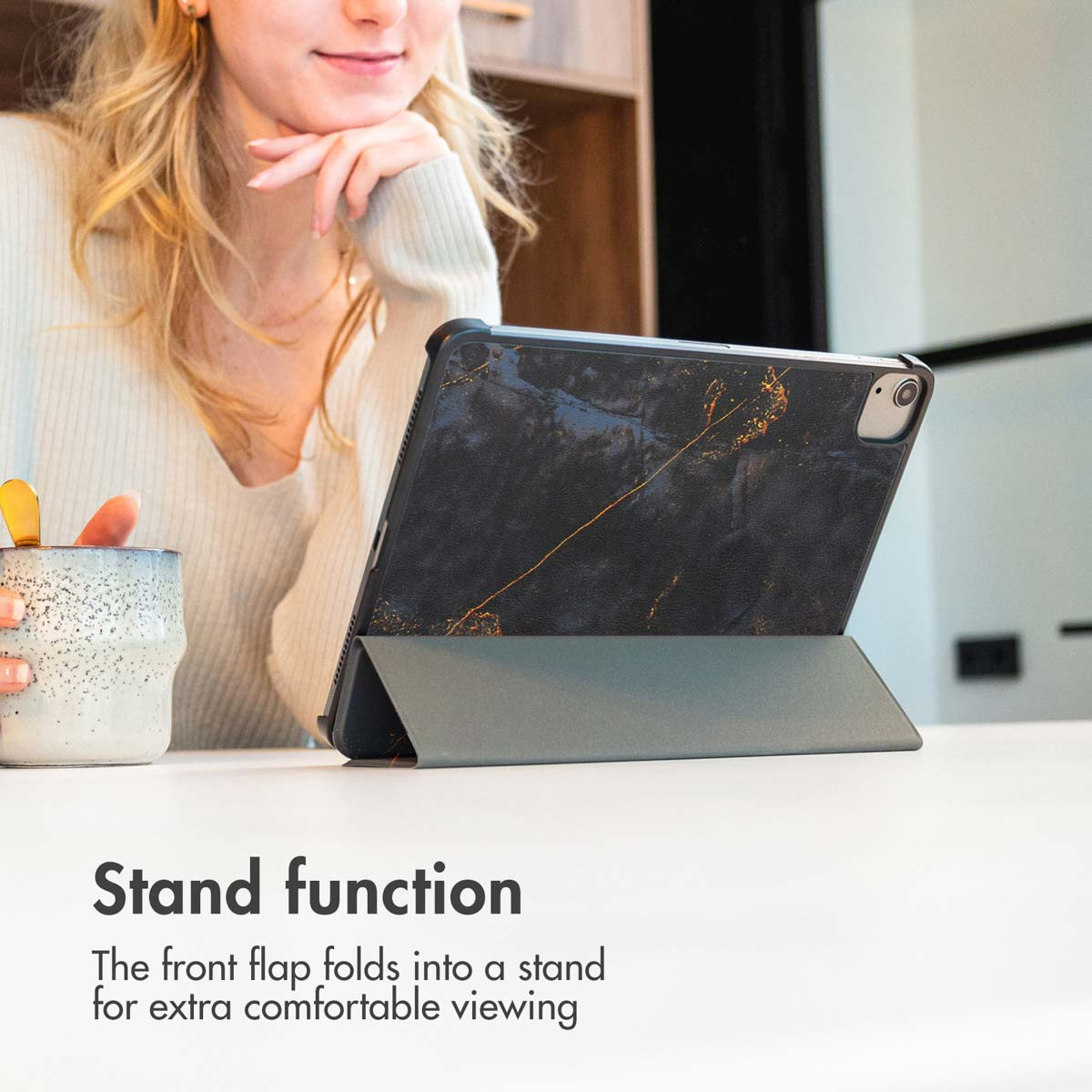 Une femme blonde est assise à une table avec une tablette dans un étui de protection noir faisant office de support.