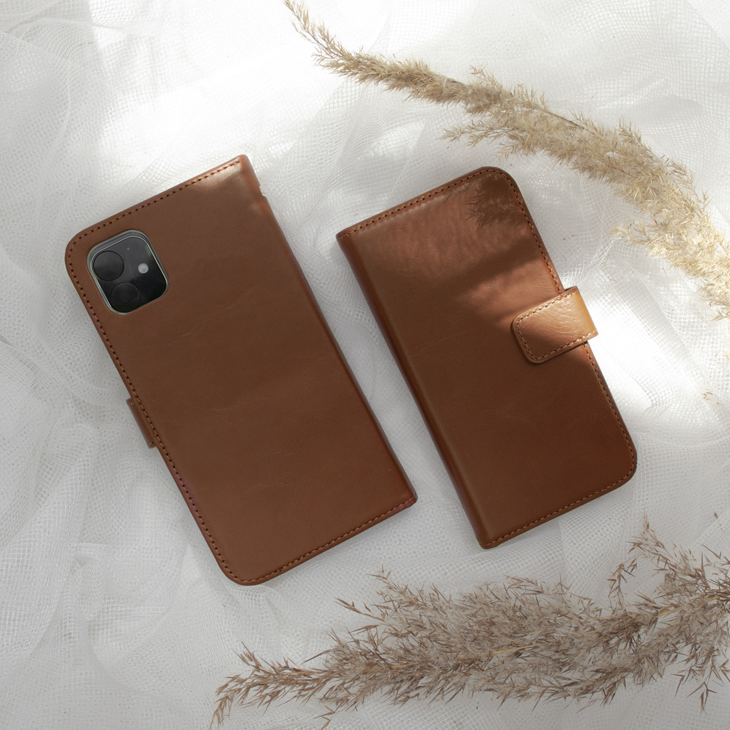 Due custodie per cellulare in pelle marrone su tessuto bianco con erba della pampa.