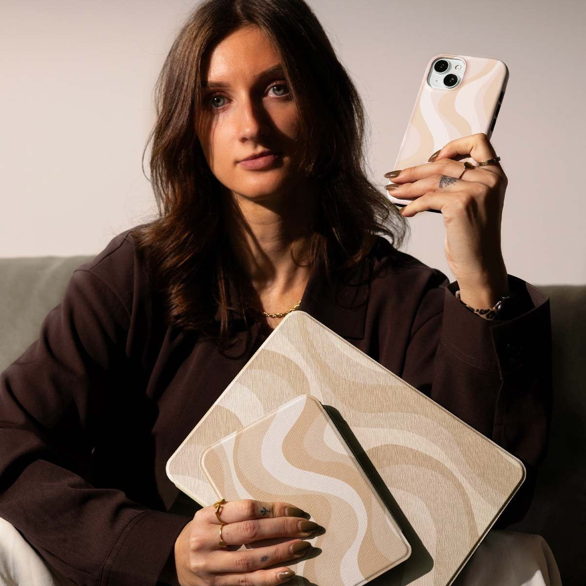Una donna in marrone tiene uno smartphone e custodie con motivi a onde beige.