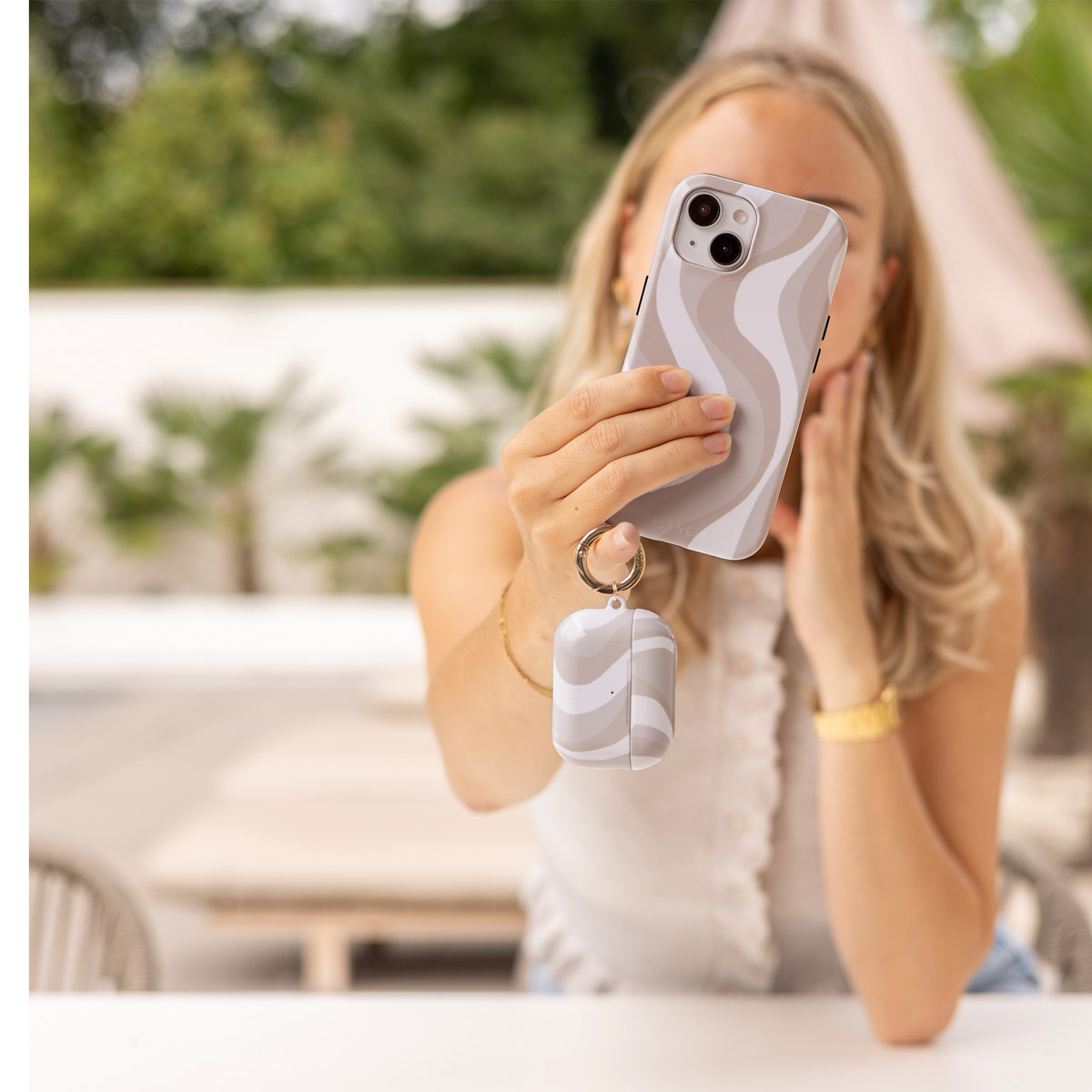 Una donna tiene in mano un telefono con custodia abbinata e custodia per auricolari.