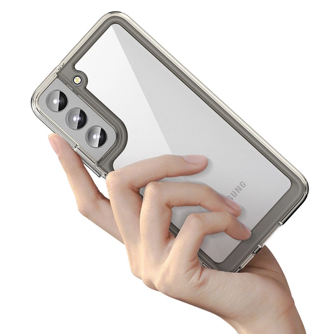 Una mano tiene uno smartphone argento con custodia trasparente e tripla fotocamera.