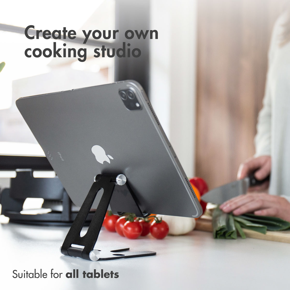 Un tablet su un supporto in cucina, con qualcuno che taglia verdure sullo sfondo.